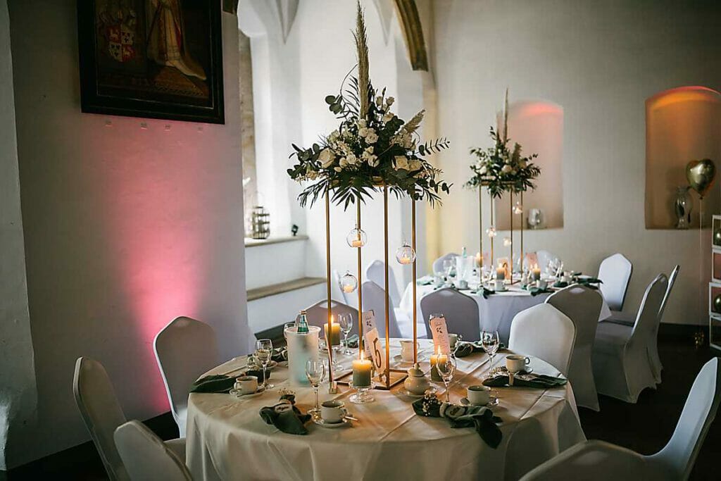 Elegante Hochzeitstafel mit weißem Leinen, grünen Servietten, Gläsern und hohen Blumenkränzen mit hängenden Glaskugeln - perfekt gestylt von einer Hochzeitsplanerin in Leipzig und Usedom für eine romantische, intime Atmosphäre.